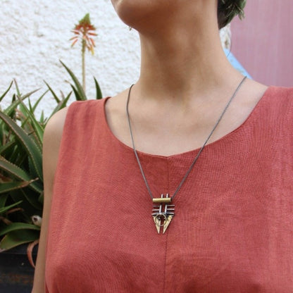 A silver and brass pendant necklace with a chain, featuring a warrior or praying mantis design.