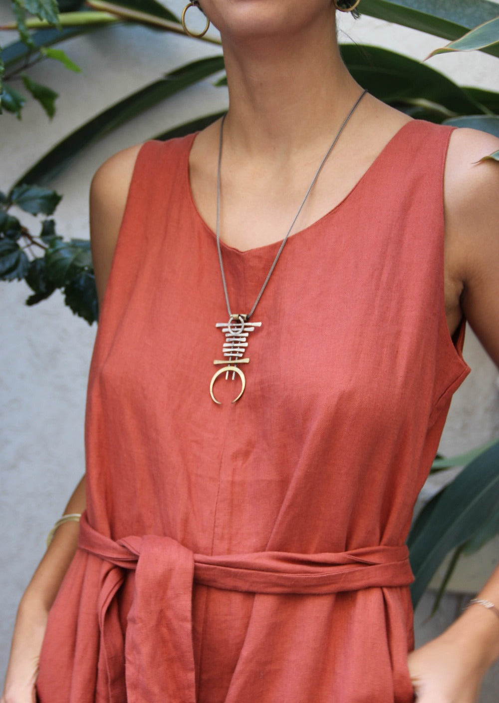 A silver and brass necklace with a geometric pendant, featuring a chain with small bell-like charms and a larger brass ring pendant.