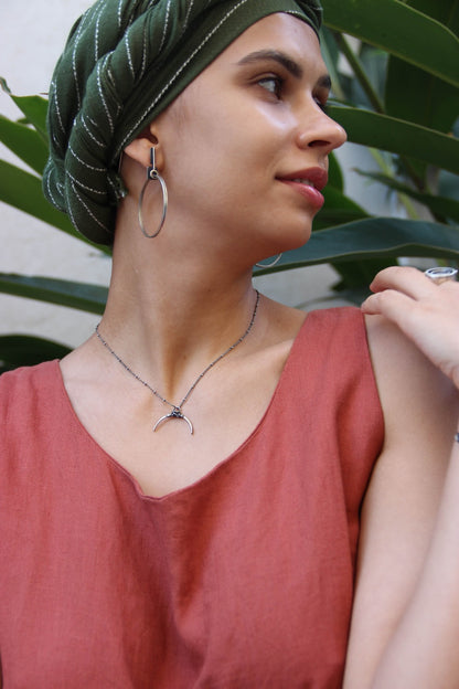 A silver necklace with a crescent-shaped pendant, featuring a chain with a series of small bell-like charms attached to it.