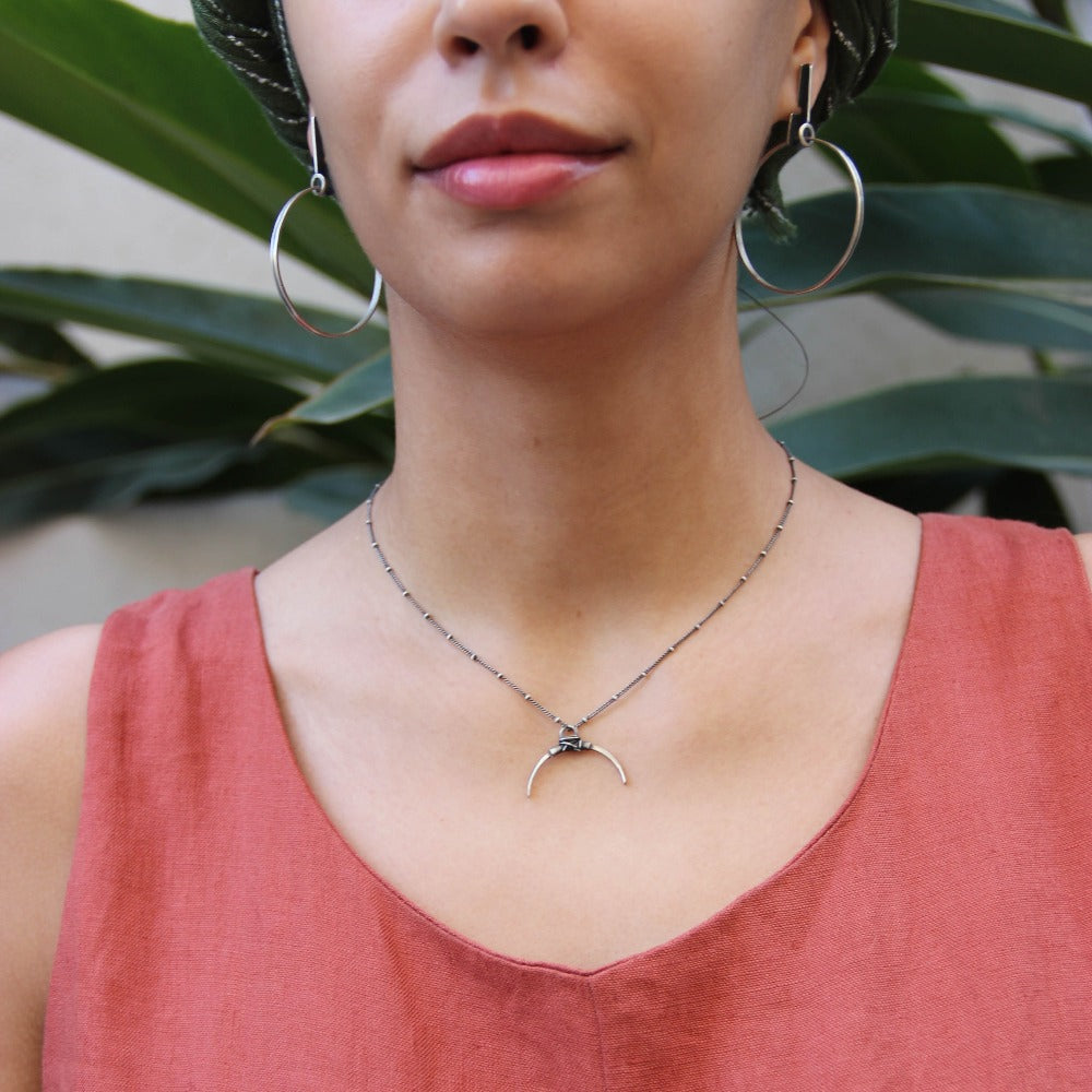 A silver necklace with a crescent-shaped pendant, featuring a chain with a series of small bell-like charms attached to it.