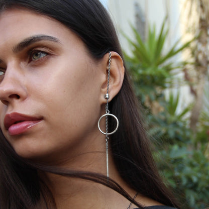 A pair of silver hoop earrings, one with a dangling tube design and the other with a chain hoop design, both made of sterling silver with a brushed finish.