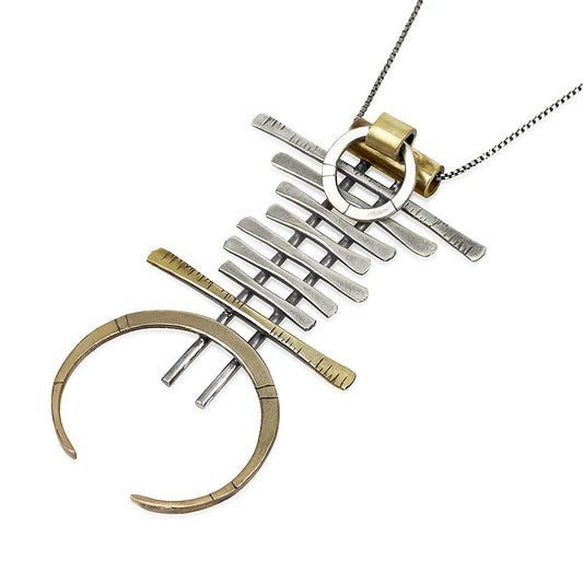 A silver and brass necklace with a geometric pendant, featuring a chain with small bell-like charms and a larger brass ring pendant.