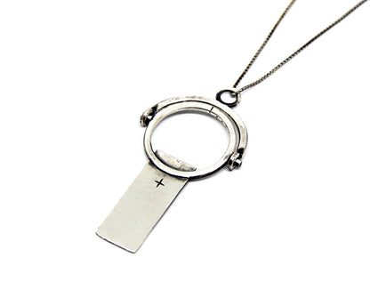 A sterling silver necklace with a magnifying glass pendant and a cross on the chain.
