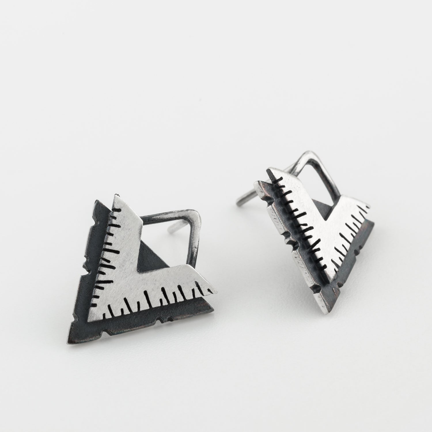 A pair of silver earrings with a geometric design, featuring a triangular shape with lines on the side, placed against a white background.