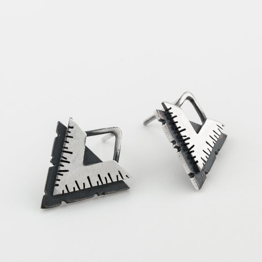 A pair of silver earrings with a geometric design, featuring a triangular shape with lines on the side, placed against a white background.