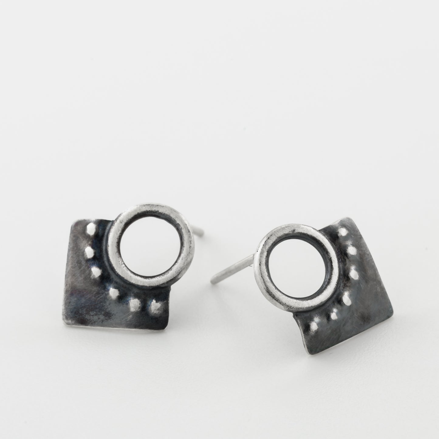 A pair of silver oxidized and brushed finish dotted rhombus earrings on a white background