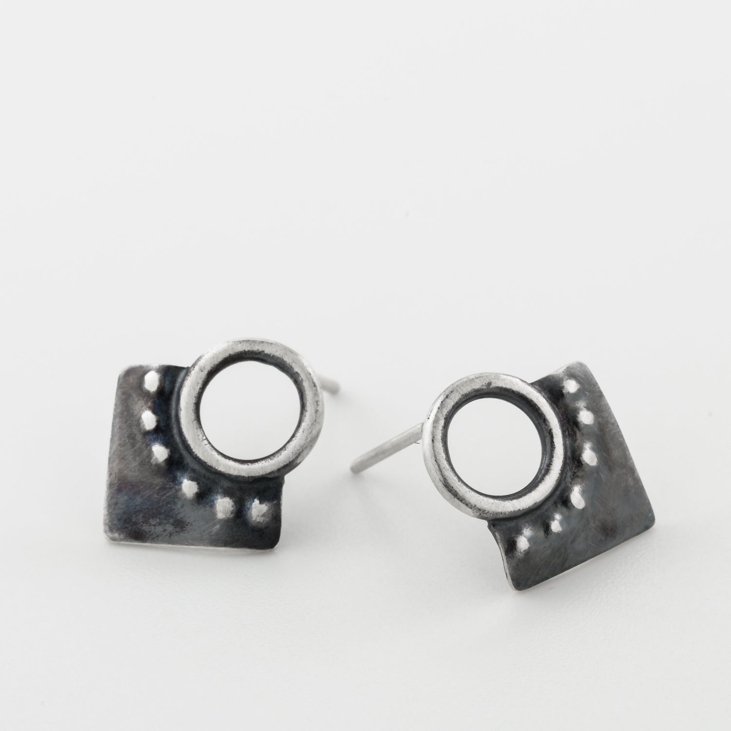 A pair of silver oxidized and brushed finish dotted rhombus earrings on a white background