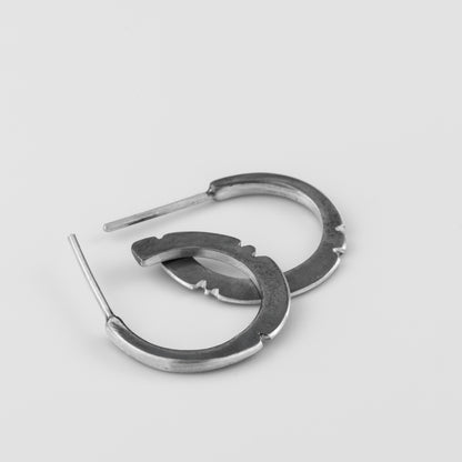 A pair of oxidized silver hoop earrings with a brushed finish, displayed against a white background.