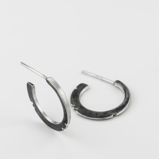 A pair of oxidized silver hoop earrings with a brushed finish, displayed against a white background.